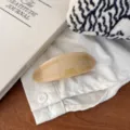 Close-up of elegant beige resin hair clip with gold lettering on white fabric background. - Melon Seed Gold Label Spring Clip / Buttercream