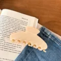 Gedetailleerd close-up van elegante minimalistische beige haarclip op boek en denimstof. - Zeven Tanden Klauw / Glimmend Melkwit