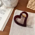 Nahaufnahme einer dunkelroten herzförmigen Haarklammer mit goldener Feder auf Leinen. - Herz Schmetterlingsschnalle / Traubenlila