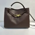 Dark brown leather handbag detail with elegant gold bow hardware and braided leather strap accent. - Coffee