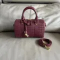 Detailed view of burgundy woven leather Boston handbag with gold tone hardware and strap. - Burgundy