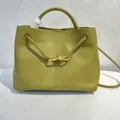 Nahaufnahme des olivgrünen Lederhandtasche mit goldenem Metallknoten und geflochtenen Riemen. - Olivgrün