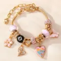 Detaillierte Nahaufnahme des goldenen DIY-Charm-Armbands mit rosa und glitzernden Anhängern. - Rosa Gitter Schmetterling Herz Stil (BZ2406fenseHB)