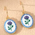 Goldfarbene Creolen mit ovalen Emaille-Anhängern, blauem Rosen- und gepunktetem Rand-Design. - Blaue Rose