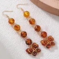 Nahaufnahme der retro bernsteinfarbenen Perlenohrhänger mit goldenen Schmetterlingsanhängern. - Schmetterling (EZ5795hudie) / Bernstein Schmetterlings-Stil