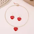 Detail shot of gold chain necklace and earrings set featuring red heart pendants with XOXO print. - Heart Shape