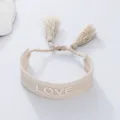 Detail shot of beige woven braided couple bracelet featuring decorative tassels and love lettering. - Beige