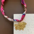 Nahaufnahme Detail einer bunten geflochtenen Stoffkordelkette mit einzigartigem goldenen Blumenanhänger. - Gold