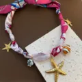 Detailaufnahme der süßen maritimen Charm-Stoffbandkette mit Seestern- und Fischanhängern. - Mehrfarbig