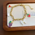 Gold-plated titanium steel charm bracelet featuring cute fruit and bow pendants for women. - Grape Bracelet (05-E22) / Gold