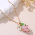 Close-up detail of sweet pink resin strawberry and white flower pendant necklace, elegant gold chain. - Pink Strawberry