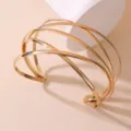 Nahaufnahme eines stilvollen goldenen Metall Mehrschicht Kreuz Armreifs mit glänzendem Finish. - Mehrschichtiger Rundstab Kreuz Stil (BZ2152-I)