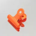 Detalle de primer plano de clip metalico naranja brillante sobre fondo de superficie reflectante. - Naranja