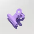 Primer plano detallado de un sujetapapeles de metal morado colocado en superficie reflectante. - Violeta Claro