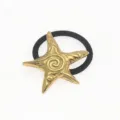 Primer plano detallado de un adorno de estrella de mar dorada en goma de pelo negra. - Dorado