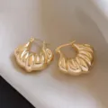 Detailed close-up of chunky gold hoop earrings with unique textured design on soft silk. - Gold