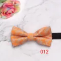 Close-up detail view of orange floral patterned men's bow tie with black strap on marble. - Orange