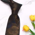 Close-up detail of a dark brown floral jacquard men necktie on white marble background. - Style F