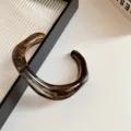 Detail of the stylish acrylic irregular geometric open bangle, showing its unique brown texture. - Black