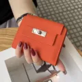 Oranger Lederkurzgeldbörse mit Metallschloss-Klappendesign, kompakt, stilvolle Alltagstasche. - Orange