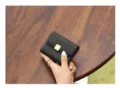 Primer plano detallado de un mini monedero de cuero negro minimalista con broche dorado. - Negro