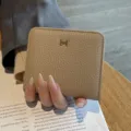 Kompakte, beige Leder-Geldbörse für Damen mit elegantem Metall-H-Verschluss und Narbenstruktur. - Grau