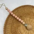 Silicone pacifier clip detail shot, featuring pink beads and wooden parts for baby teething. - Pink