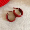 Nahaufnahme von dunkelroten dicken Creolen auf strukturiertem beigen Hintergrund. - Rote Creolen (Silberstift)