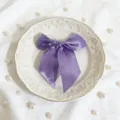 Dettaglio fiocco in raso viola, elegante fiocco decorativo su piatto bianco con perle. - Viola