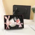 Coffret cadeau noir élégant avec lapin en peluche rose et bouquet de fleurs pour fêtes. - Boîte cadeau noire avec nœud à bordure dorée + raphia + carte + bouquet + guirlande lumineuse + lapin