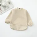 Vista detallada del babero impermeable beige para bebés, con mangas largas y bolsillo recogemigas. - Beige