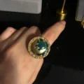 Primer plano detallado de un anillo con diseño de planeta, esmalte verde y cristales. - Anillo (FM30)
