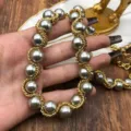 Primer plano detallado de un collar vintage con cadena dorada trenzada y perlas grises elegantes. - Collar (HE116) / Dorado