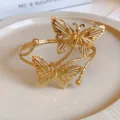 Dettaglio ravvicinato del bracciale rigido aperto in metallo dorato con farfalla traforata. - Stile Doppia Farfalla Cava (Stile 3)