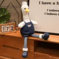 Simpatico giocattolo di papera di peluche a gambe lunghe con salopette in denim per decoro. - Anatra dalle gambe lunghe con salopette di jeans