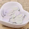 Close-up of 15mm white laser round sequins with hole in heart bowl, craft DIY accessory detail. - Iridescent Solid White