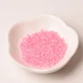 Gros plan de perles de rocailles en verre rose de 2mm dans un bol blanc, idéal pour bijoux DIY. - Rose