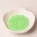 Detail view of 2mm light green glass seed beads in a white dish, ideal for DIY jewelry making. - Fruit Green