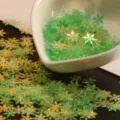 Gros plan détaillé de paillettes flocon vert irisé sortant d'un bol cœur pour loisirs créatifs. - Vert clair