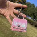 Dettaglio di un portachiavi mini borsa con paillettes rosa tenuto all'aperto al sole - portachiavi per borse / Ricamo Piatto Rosa