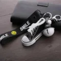 Détail du porte-clés mini chaussure en toile avec sangle sourire et grand pendentif clochette. - Noir