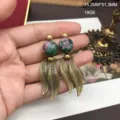 Vista detallada de pendientes dorados retro con cuentas de piedra verde y colgantes de metal. - Pendiente de Rubí en Zoisita