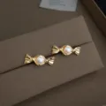 Nahaufnahme von goldenen Perlen-Ohrringen in Bonbon-Form auf braunem Samt, elegantes Schmuckstück - Süßigkeiten Perle Ohrstecker (4287)