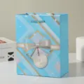 Blue gift bag detail view featuring an elegant 3D ribbon bow and decorative tag. - 18x10x23cm / Blue