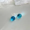 Nahaufnahme von durchsichtigen blauen Glaskugel Ohrsteckern mit filigranen Silberstiften. - Hellblau
