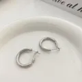 Primo piano dettagliato di eleganti orecchini a cerchio in metallo argentato su piatto bianco. - Argento Fedina Semplice