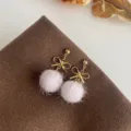 Süsser pinker Plüschkugel Ohrring Detailansicht mit goldener Schleife auf braunem Stoff. - Goldene große Schleife Haarball Stil (C-428) / Rosa