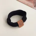 Detailed close-up shot of a black elastic hair tie featuring a cute brown bear leather patch. - Black Bear Tag Style (3375)