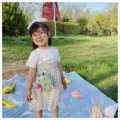 Detailed outdoor shot of a cute sequin ladybug crossbody bag worn by a child in a park setting. - Light Green