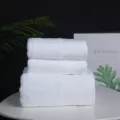 Detailed view of white cotton hotel towels set neatly stacked on table with green leaf. - Large Square / 32*32cm (60g) / White